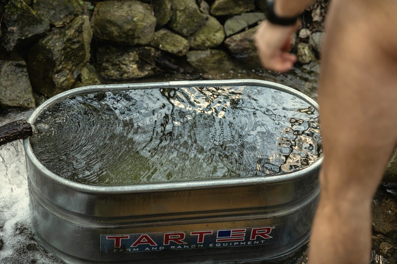 Close-up of water rippling in a galvanised stock tank cold plunge beside a rocky stream