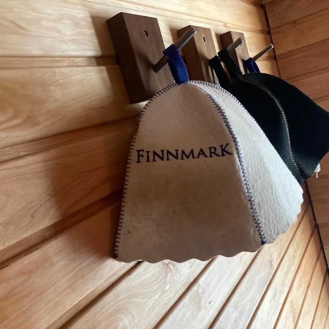 Felt sauna hats hanging on wooden hooks inside a timber-lined sauna cabin