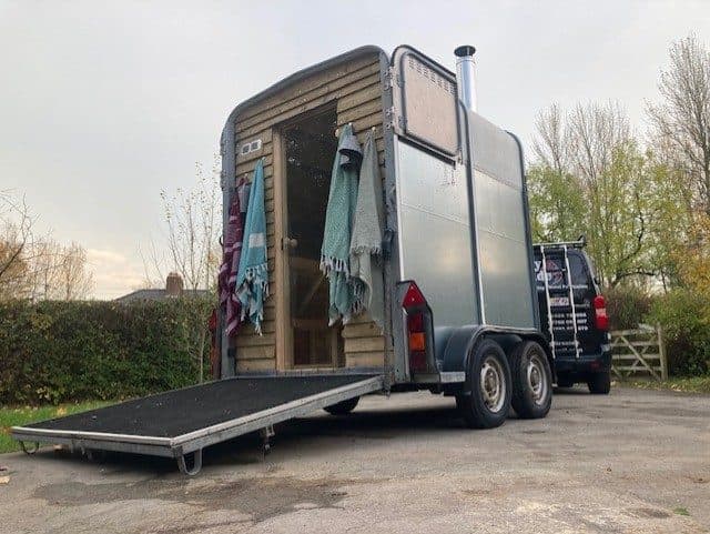 Horsebox sauna with open ramp and towels parked in a rural setting with hedgerow behind