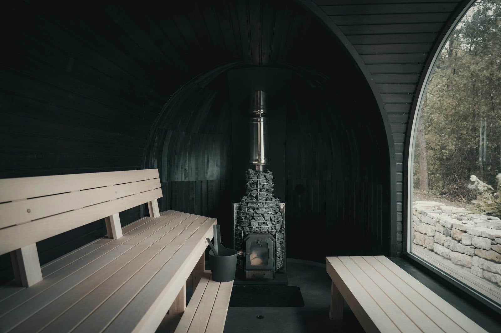Interior of a pod sauna with dark-stained timber and a wood stove