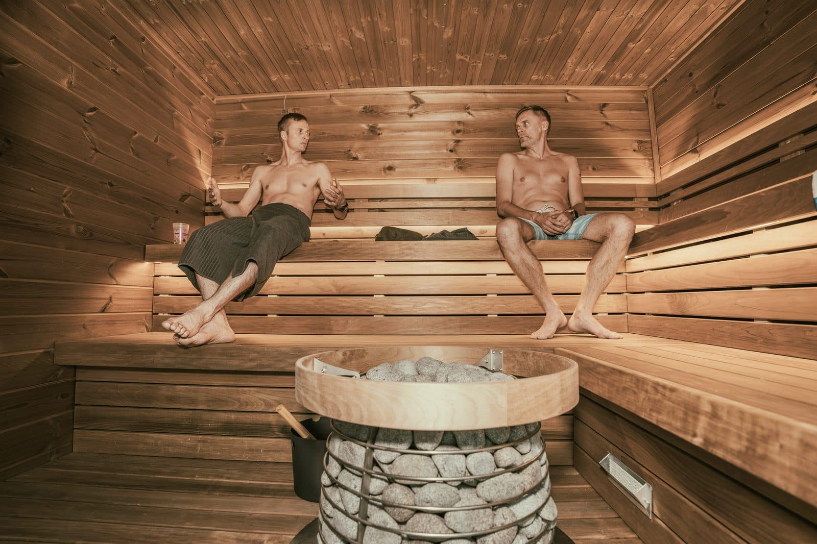 Two people relaxing on tiered timber benches inside a sauna