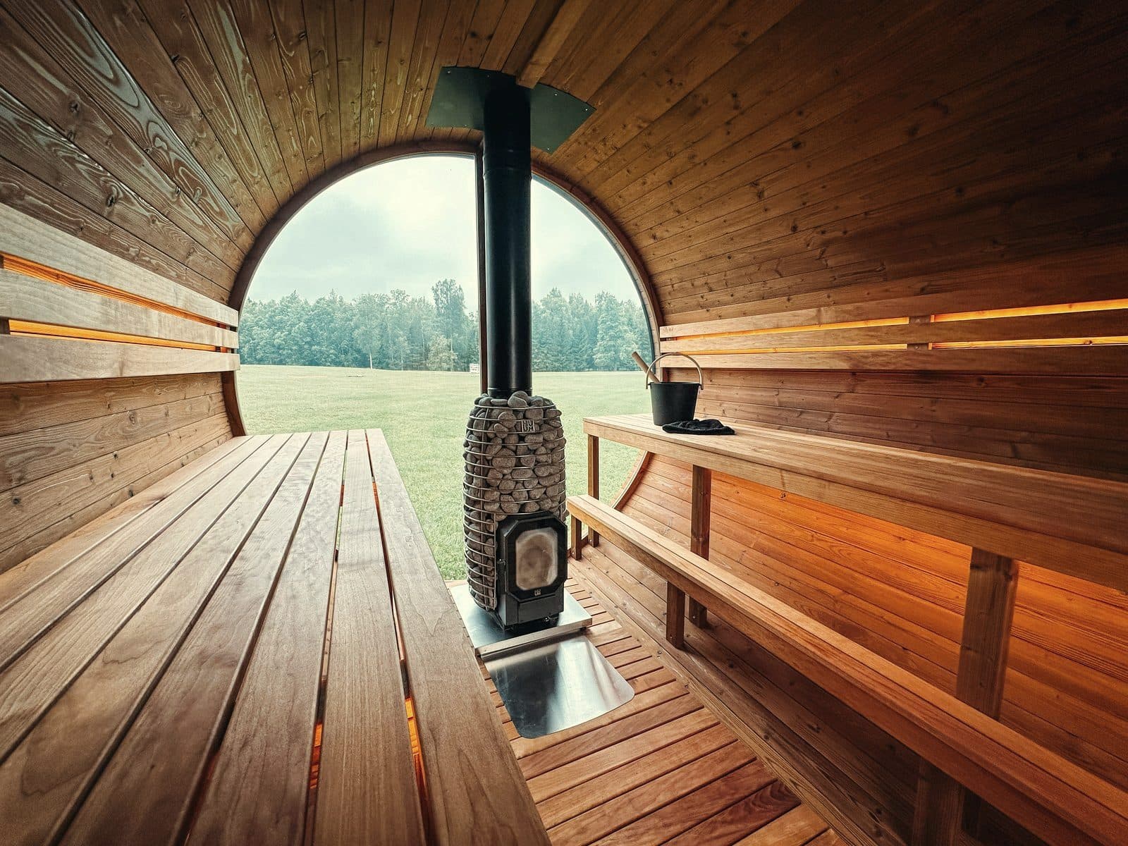 Inside a barrel sauna showing timber benches and a wood-fired stove