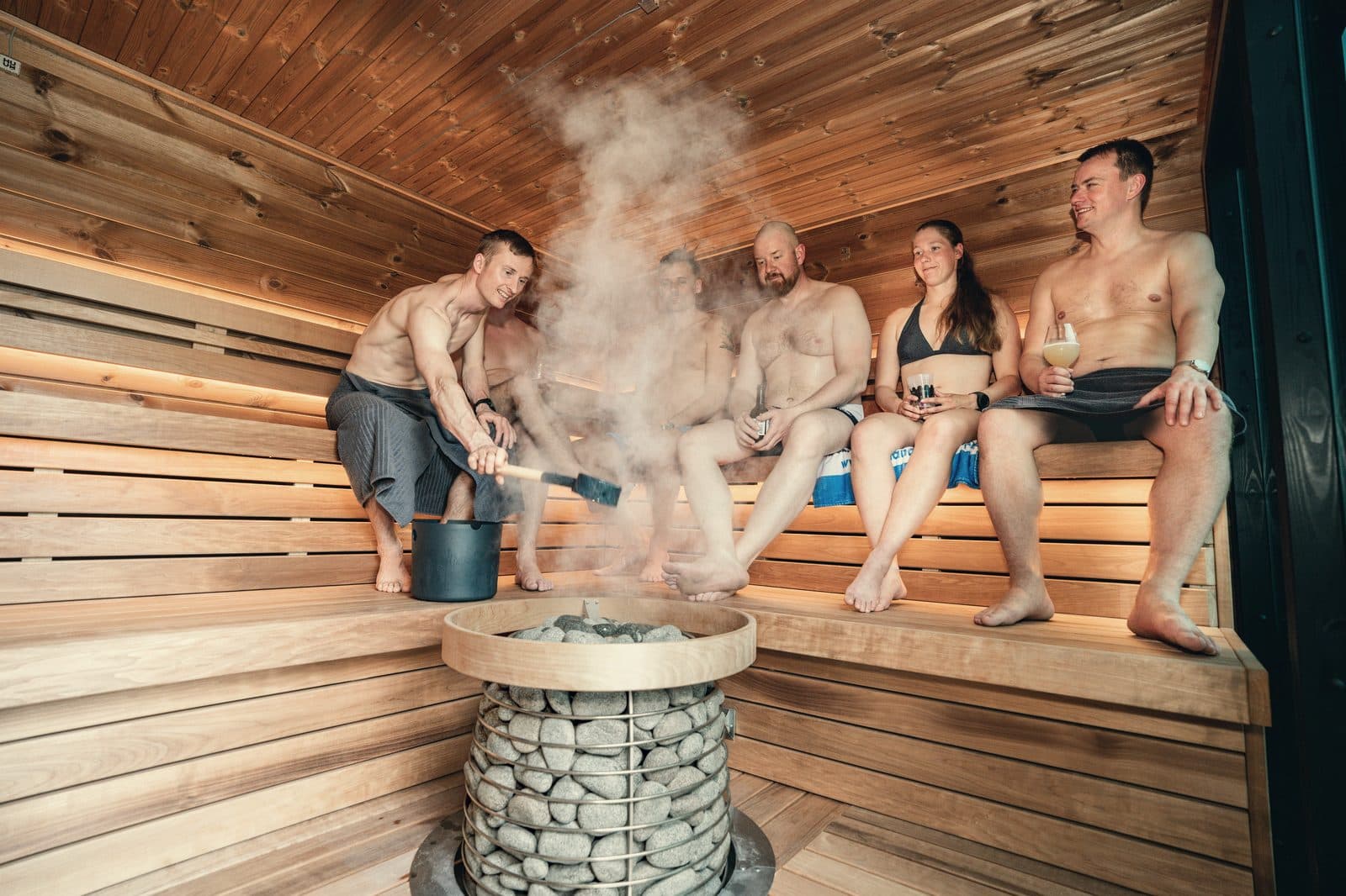 Group on tiered sauna benches with steam rising from a stone heater