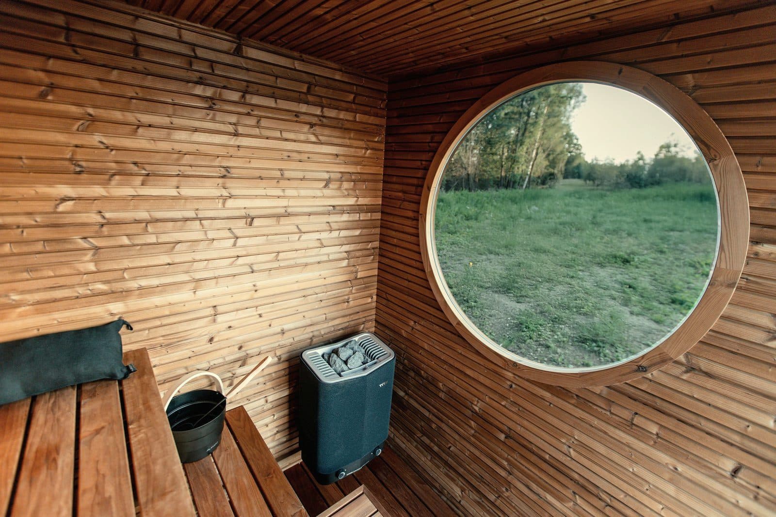 Sauna interior with electric heater and round window to greenery